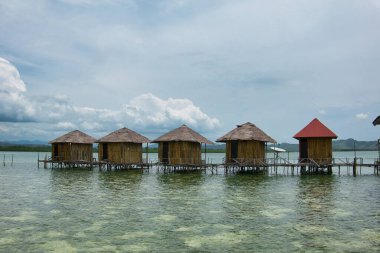 Seram, Maluku Endonezya 'nın batısında, mavi ve bulutlu gökyüzüne karşı uzanan çok sayıda geleneksel evden oluşan denizin ortasındaki tatil köyü manzarası
