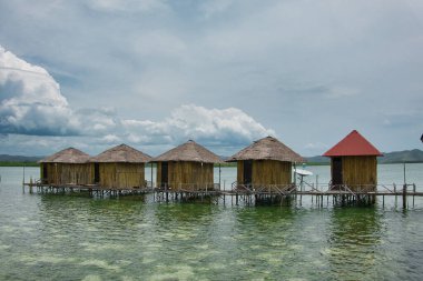 Seram, Maluku Endonezya 'nın batısında, mavi ve bulutlu gökyüzüne karşı uzanan çok sayıda geleneksel evden oluşan denizin ortasındaki tatil köyü manzarası