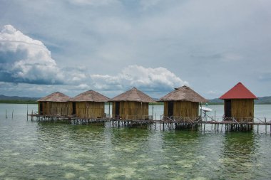 Seram, Maluku Endonezya 'nın batısında, mavi ve bulutlu gökyüzüne karşı uzanan çok sayıda geleneksel evden oluşan denizin ortasındaki tatil köyü manzarası
