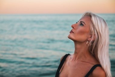 Gün batımında sahilde gökyüzüne bakan güzel bir kadın.