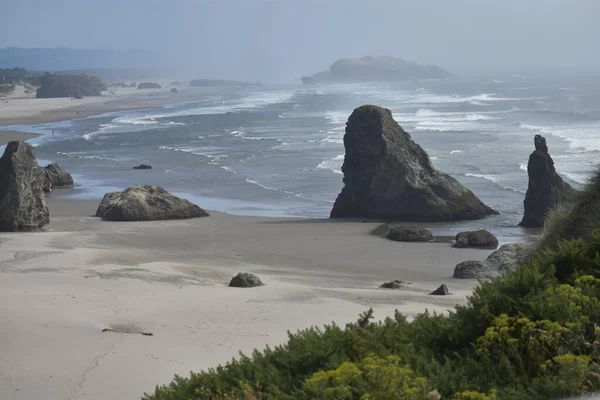 遠くの波とブラシの前景を持つオレゴン海岸の崖からの岩やビーチ — ストック写真