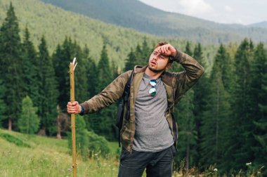 Yürüyüşe çıkmış yorgun susamış bir adam elinde bir sopayla dağlarda duruyor, kafasını çeviriyor ve terini eliyle siliyor. Dağlarda yorgun bir turistin portresi