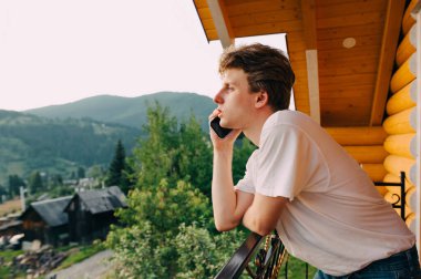 Genç bir hippi, dağlarda bir balkonda rahatlarken akıllı telefondan iletişim kuruyor. Turist telefonda konuşuyor. Dağlardaki bir otel odasının balkonunda..
