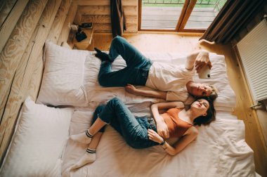 Birbirine aşık güzel genç bir çift odunsu bir dairede yatakta uzanıyor ve akıllı telefondan selfie çekiyor. Bir kadın ve bir erkek otel odasındaki yatakta selfie çekiyorlar. Üst görünüm