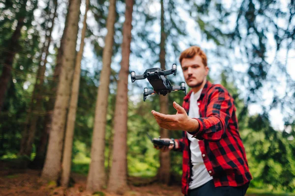 Young man stands in the woods and launches a drone into the air with his hands. Focus on the drone on the background of a man trying to catch his hand. Drone flight in the woods.