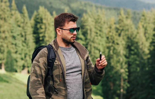 Yetişkin bir adam dağlarda oturur ve elektronik bir sigarayla dinlenir. Dağlarda yürüyüş yapan bir yürüyüşçü bir elektronik sigara içer. Tütünün buharlaşması.