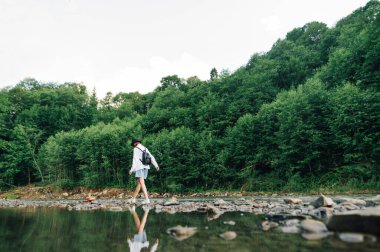 Gündelik giysiler içinde şık bir bayan ve bir sırt çantası dağ nehrinde yürüyor, kayaların üzerinde yürüyor. Dağlarda turizm