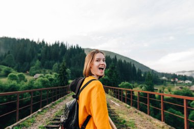 Bir dağ köprüsünde sıradan giysiler içinde komik bir kadının portresi. Şaşırmış bir yüzle kameraya bakıyor ve gülümsüyor..