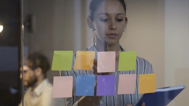 Young woman working in the office and sticking notes on a glass wall — Stock Video