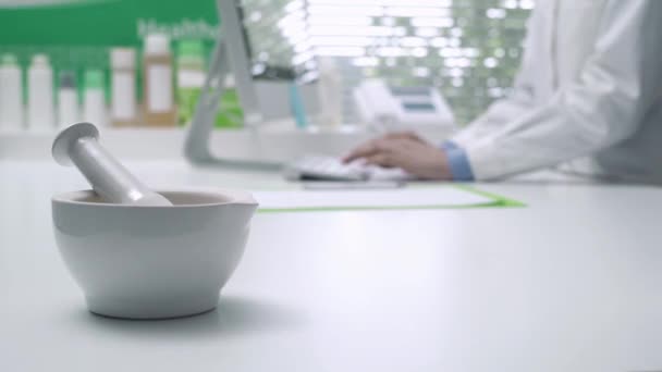 Professional pharmacist working with a computer and connecting online, mortar and pestle on the foreground: medicine and technology concept