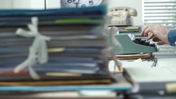 Empleado escribiendo con una máquina de escribir y montones de papeleo — Vídeo de stock