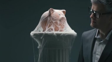 Örümcek ağları ile piggy banka üzerinde üfleme hayal kırıklığına sinirli işadamı: başarısız uzun vadeli yatırım fonları ve dondurulmuş banka hesap kavramı