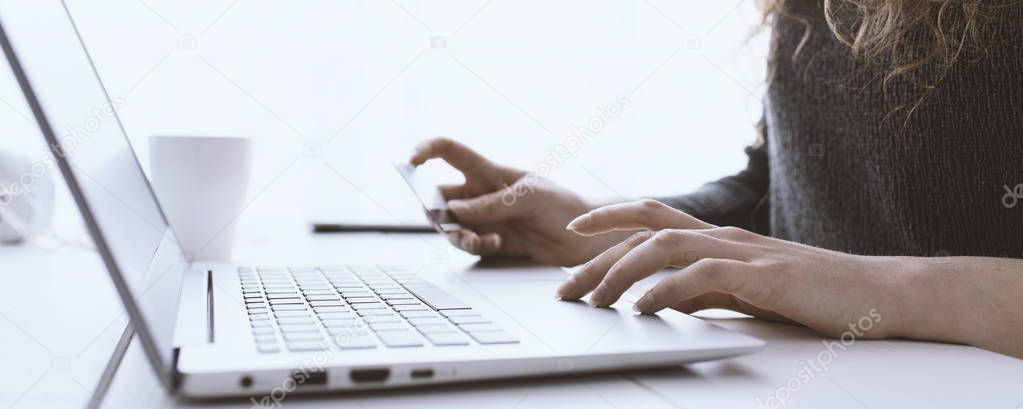 Woman doing online shopping using her laptop and a credit card, hands close up, e-commerce and online banking concept