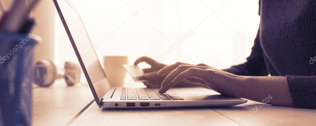 Woman doing online shopping using her laptop and a credit card, hands close up, e-commerce and online banking concept