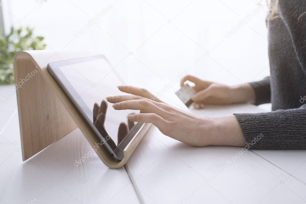 Woman using apps on a digital tablet and shopping online with a credit card, hands close up