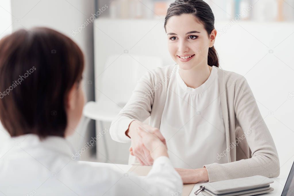 Female doctor and young smiling patient in the office, they are shaking hands