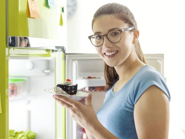 Buzdolabını açma ve lezzetli çikolata tatlı sahip mutlu bir genç kadın