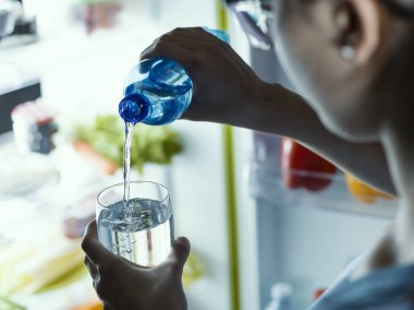 Bir şişe buzdolabından su alarak ve bir bardak dökme kadın