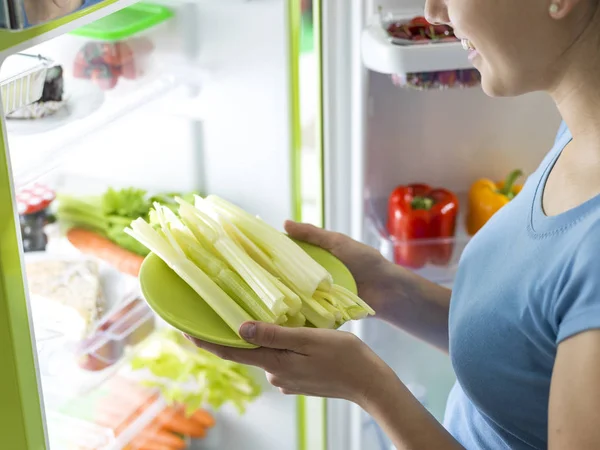 冷蔵庫の中からいくつかの新鮮なセロリをとり家で健康的なお食事を準備する女性 — ストック写真