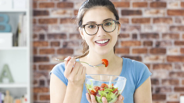 Happy young woman eating fresh salad in a bowl, healthy vegan food and dieting concept