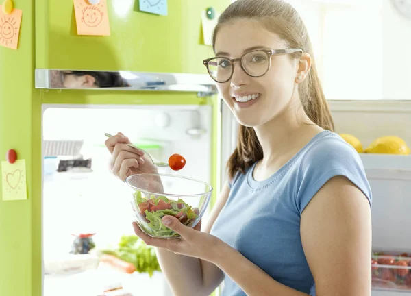 笑顔の女性健康ビーガン フード 冷蔵庫の横にあるいくつかの新鮮なサラダを食べることやダイエットの概念 — ストック写真