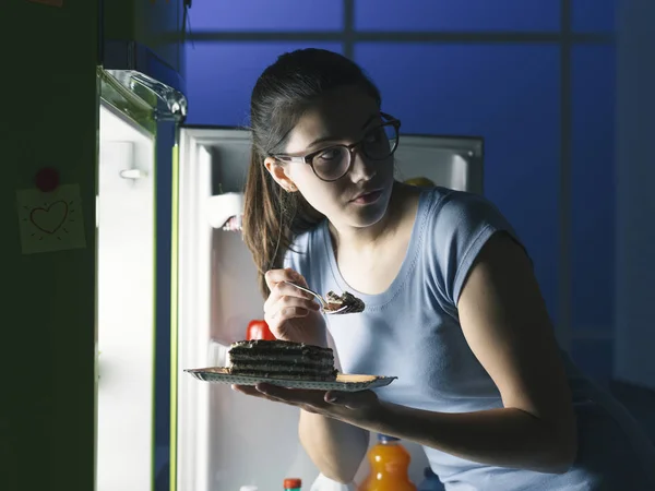 Woman in the kitchen having a late night snack, she is taking a delicious dessert from the fridge, diet fail concept