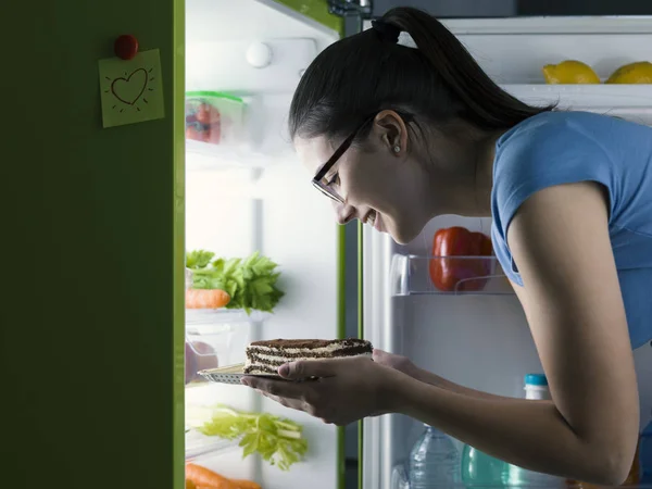 Woman in the kitchen having a late night snack, she is taking a delicious dessert from the fridge, diet fail concept
