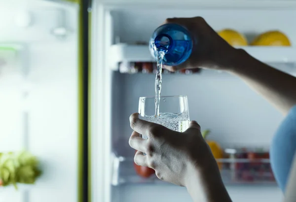 女人从冰箱里拿出一瓶水倒入玻璃杯中 — 图库照片