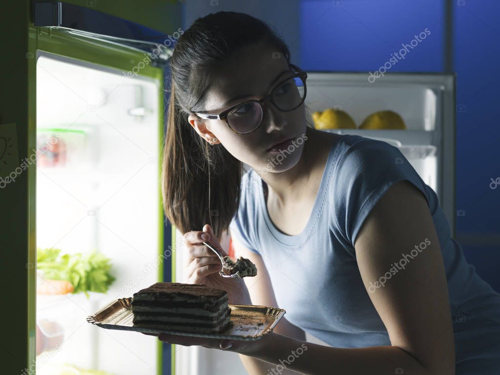 Woman in the kitchen having a late night snack, she is taking a delicious dessert from the fridge, diet fail concept