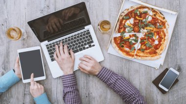 Ofis çalışanları ofiste yemek molası veriyorlar, pizza yiyorlar, dizüstü bilgisayar ve dijital tablet kullanıyorlar, düz konum alıyorlar.