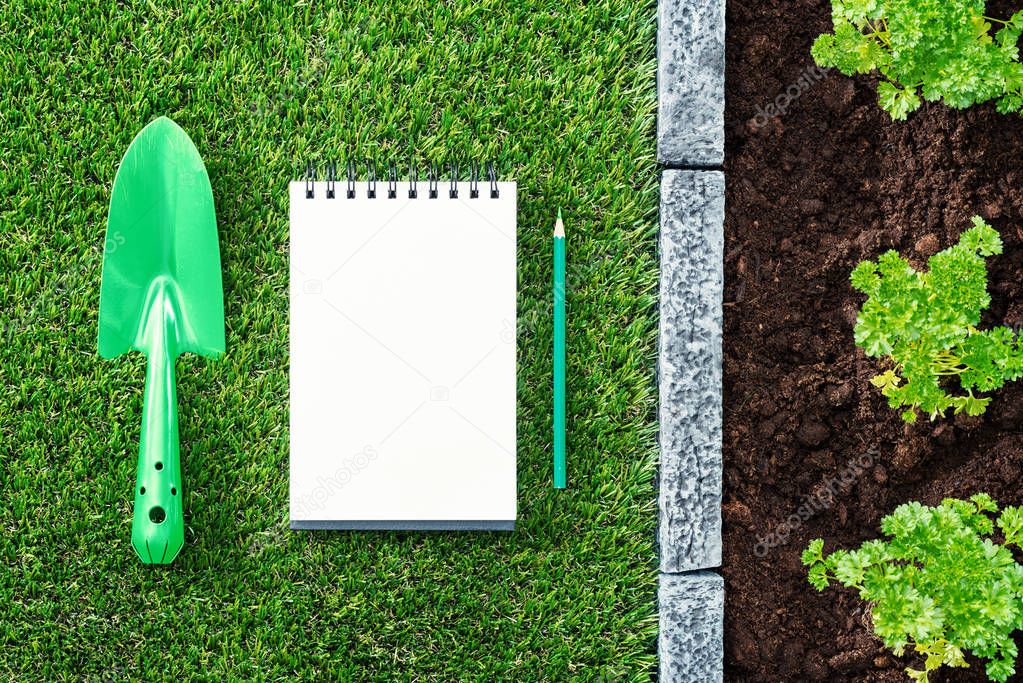 Gardener's to-do list: blank notepad, shovel and plants growing on the soil