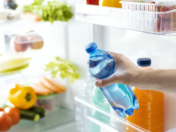 Frau holt eine Flasche Wasser aus dem Kühlschrank — Stockfoto