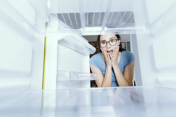 Verzweifelte Frau blickt in ihren leeren Kühlschrank — Stockfoto