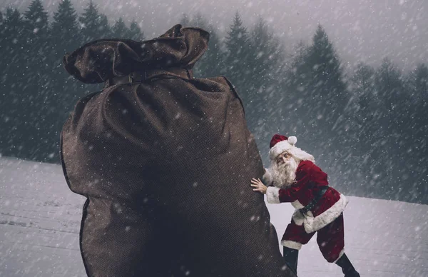 Santa empujando un enorme saco con regalos bajo la nieve — Foto de Stock