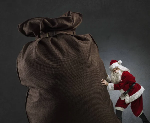 Santa empujando un enorme saco con regalos — Foto de Stock