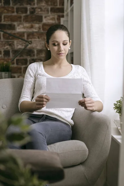 Jonge vrouw zitten in de woonkamer en het lezen van een brief — Stockfoto