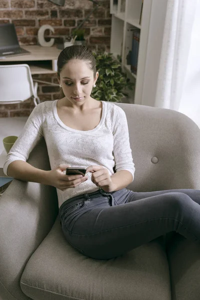 Mujer joven conectándose con su teléfono inteligente en casa — Foto de Stock