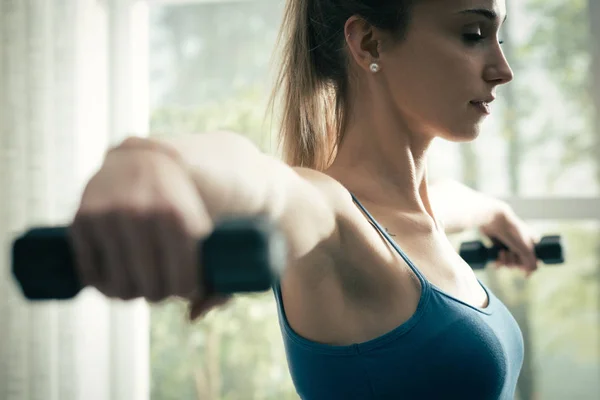 Young sporty woman exercising with dumbbells at home — Stock Photo, Image