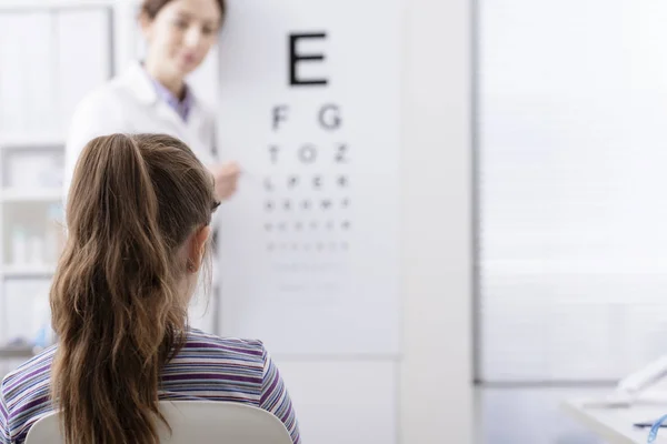 Oculista testar a visão de um paciente jovem usando um gráfico ocular — Fotografia de Stock
