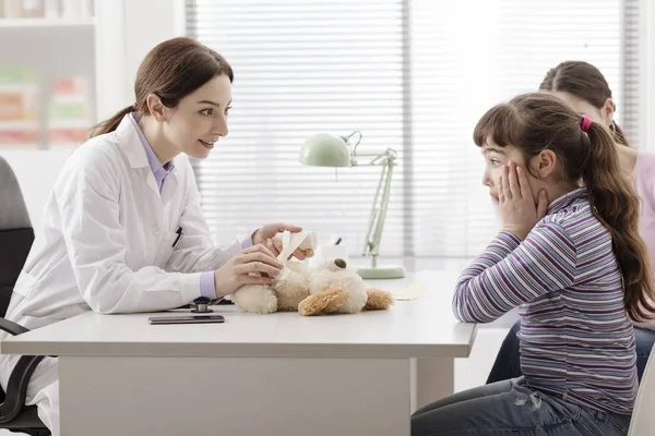 Playful doctor wrapping a girl's teddy bear with a bandage — Stock Photo, Image