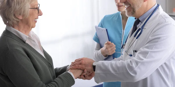 Amistoso médico profesional sosteniendo las manos de un paciente mayor — Foto de Stock