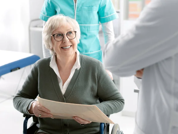 Paciente de edad avanzada en silla de ruedas con personal médico —  Fotos de Stock