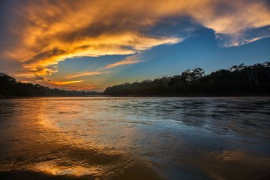 Ateşli bir günbatımı Tambopata Nehri 'nin üzerindeki gökyüzünü tutuşturarak Amazon' u altın yansımaları ve sonsuz dinginlikle resmediyor. Anne de Dios Peru.