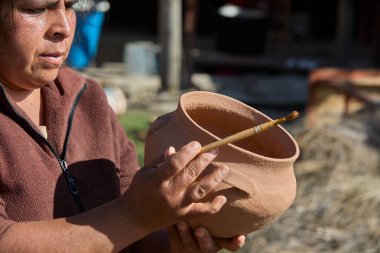 Huancas 'lı bir kadın çanak çömleğini ateş etmeden önce basit ve sembolik şekillerle dekore ediyor. Her bir jest atalarını onurlandırıyor, kilden kültür, gelenek ve zamansız And sanatının taşıyıcısına dönüşüyor..