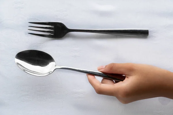 Mano de niña sosteniendo cuchara de plata y tenedor en mantel blanco alimentos —  Fotos de Stock