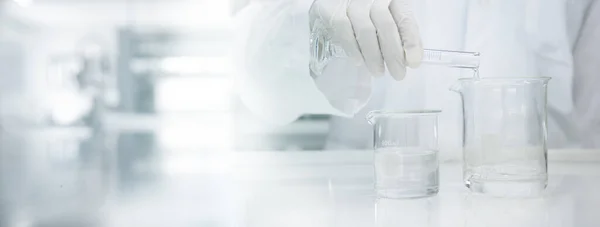 Beyaz önlüklü bilim adamı, tıbbi laboratuvar bilim afişinde suyu cam deney şişesine yerleştiriyor.
