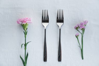 İki özdeş gümüş çatal pembe karanfil ve yemek servisi geçmişi için mor çiçek.