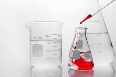 Beyaz araştırma laboratuarının arka planında cam matarada kimyasal çözelti damlası