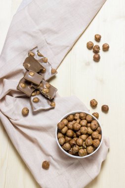 Fındık soyulmuş. Bir porselen kase. Bütün fındık ile sütlü çikolata. Çikolata parçaları. Hafif ahşap arka plan. Işık havlu.