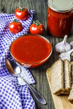 Bir cam kasede salça. Bir kavanoz içinde domates sosu. Olgun domates ve sarımsak. Damalı havlu ve kaşık. Dilimlenmiş ekmek. Unrenalized tablo. Ülke stil. Rustik